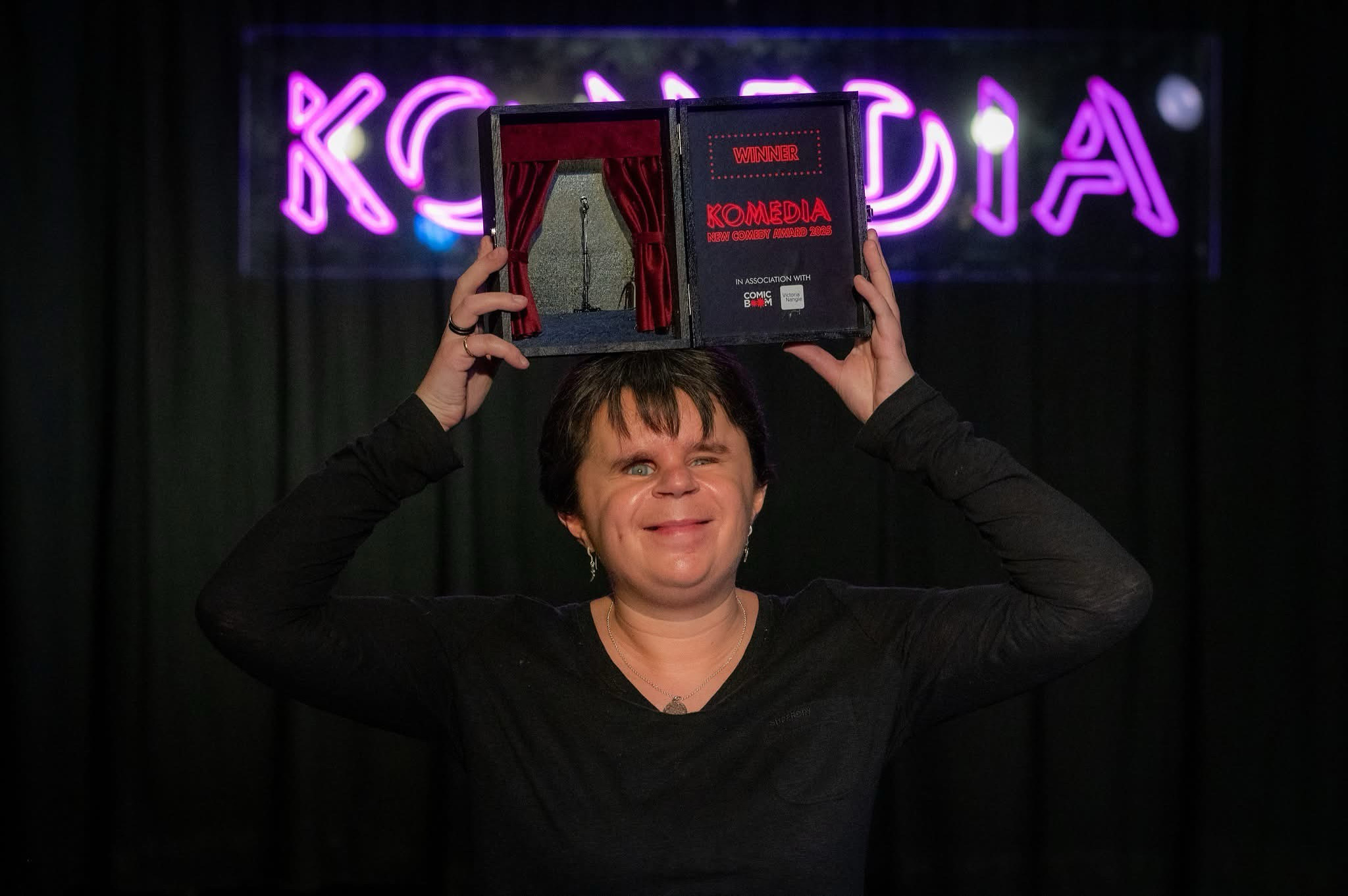 Syd holding winning award from Komedia best newcomer awards 2025 above her head.
